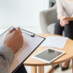 Counselor holding clipboard and listening to a patient